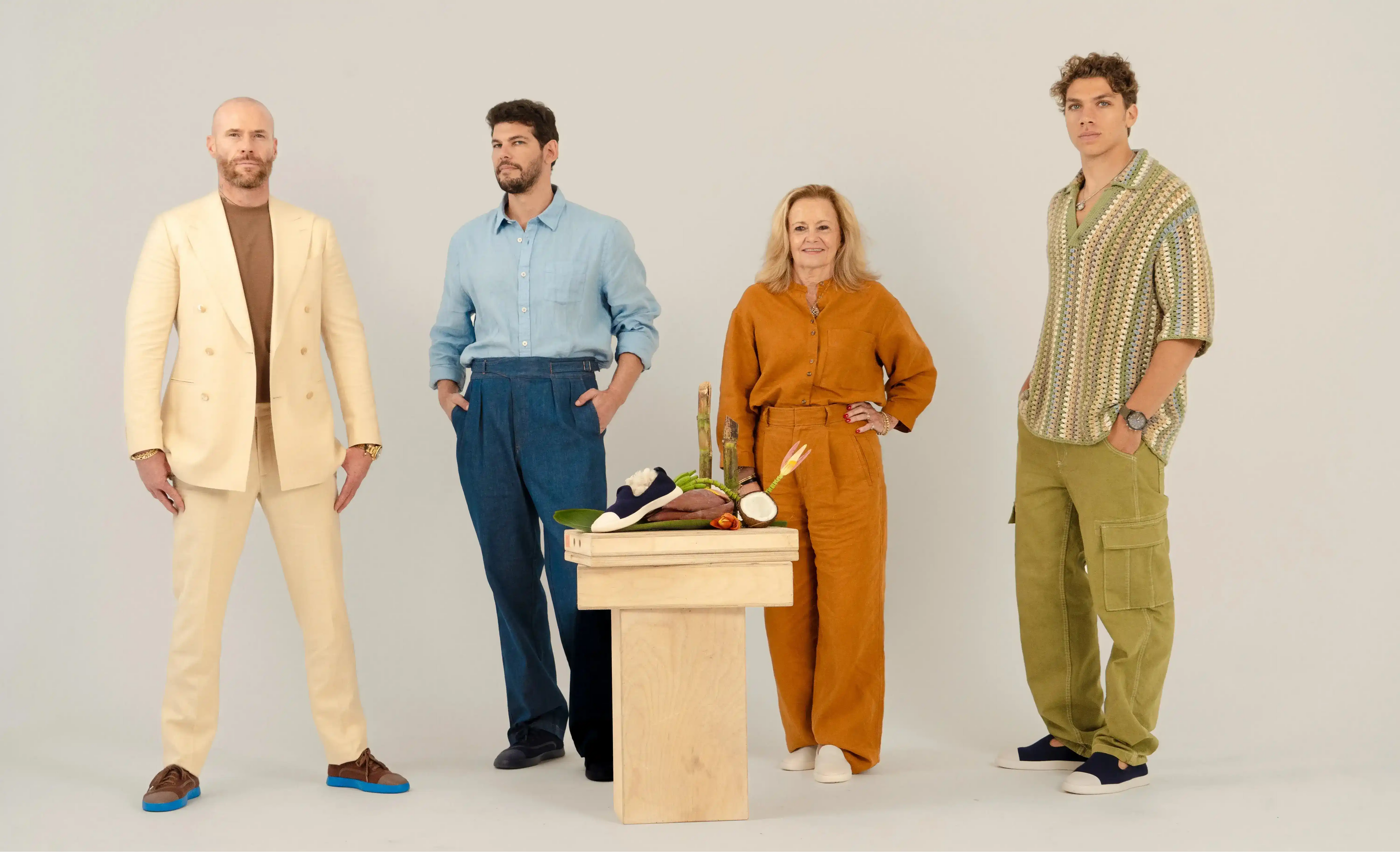 Four people standing around a wooden table with a neutral background