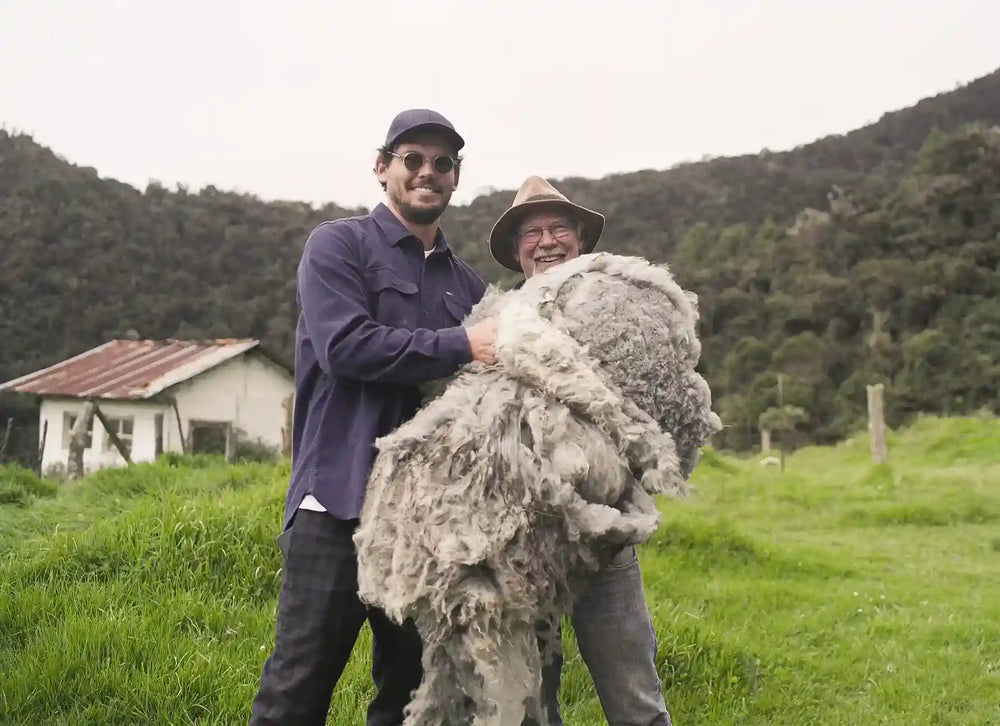 Two people holding alpaca wool in grassy field with mountains, Juntos sustainable materials.