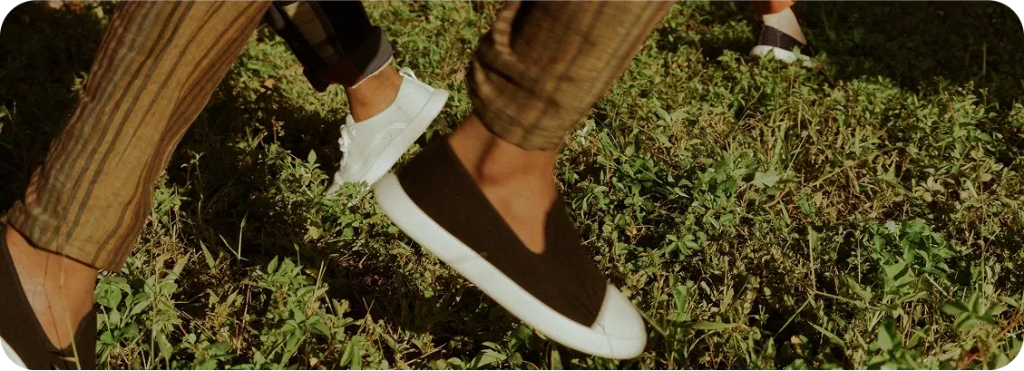 Close-up of feet wearing brown shoes with white soles on a grassy ground.