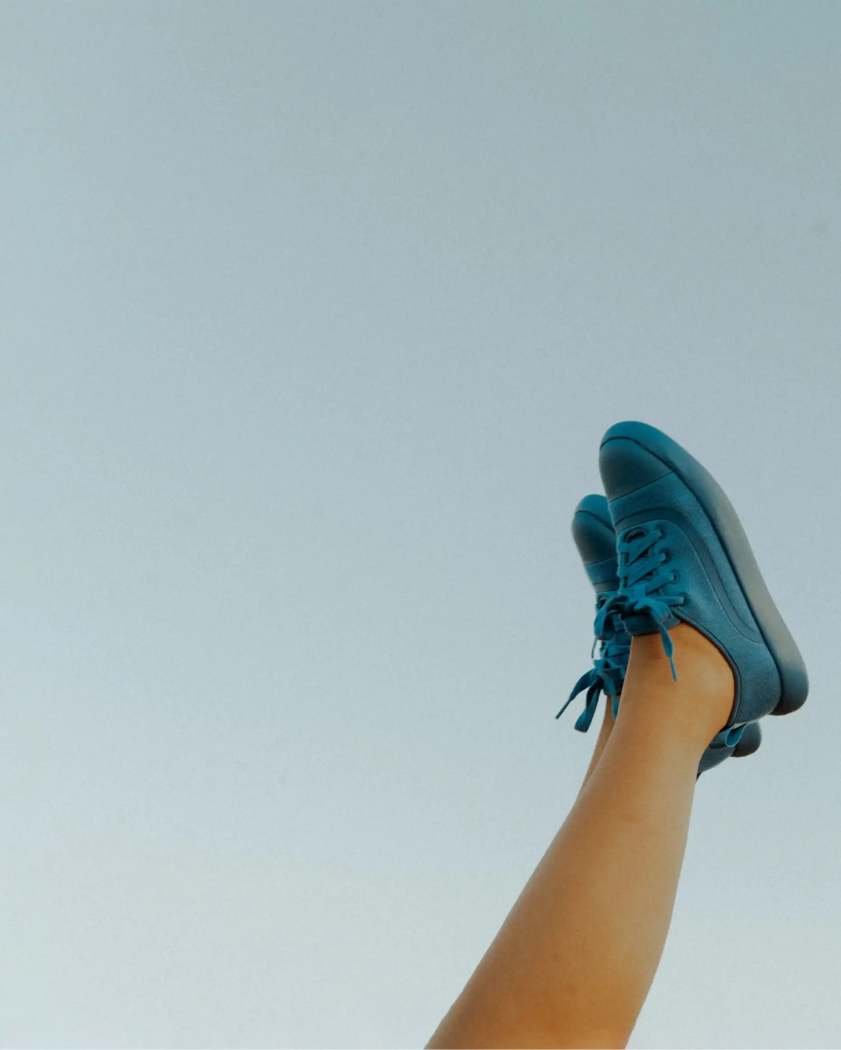 Teal sneakers being worn against a light blue sky