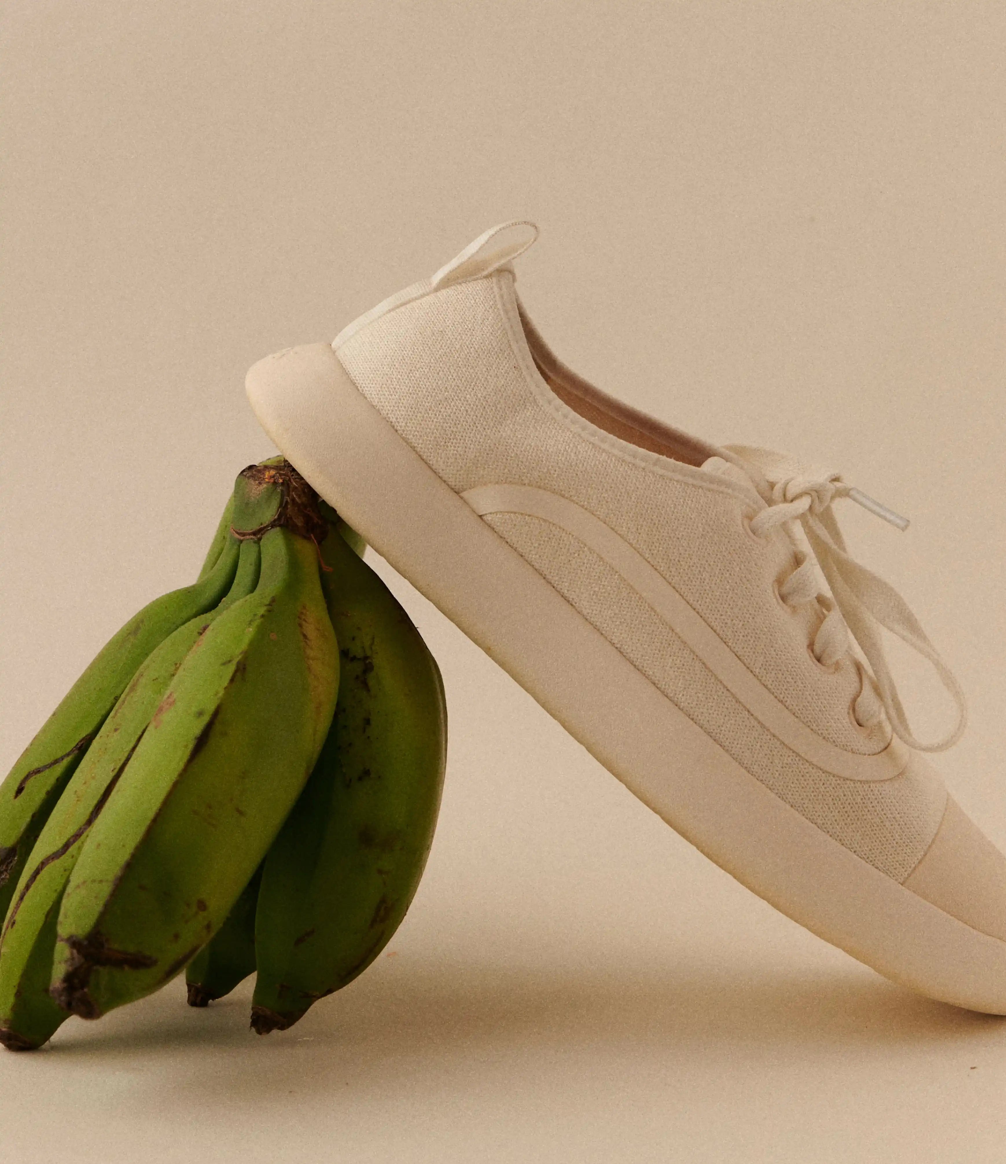 Juntos sneaker leaning against a bunch of green bananas on a beige background