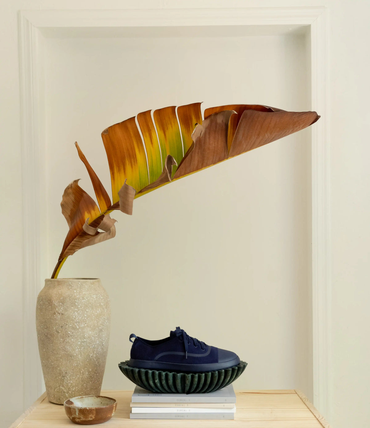 Decorative setup with a vase, plant, and shoes on a shelf against a beige wall.